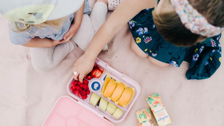 Codi Lynn's two children picking fruit from a bento box next to SunRype Fruit Plus Veggies juice boxes, from a bird's eye view