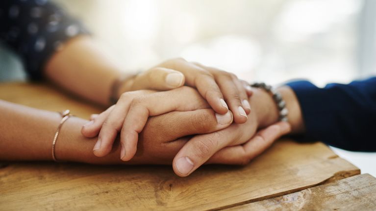 A person's hands cradling another person's hands in support
