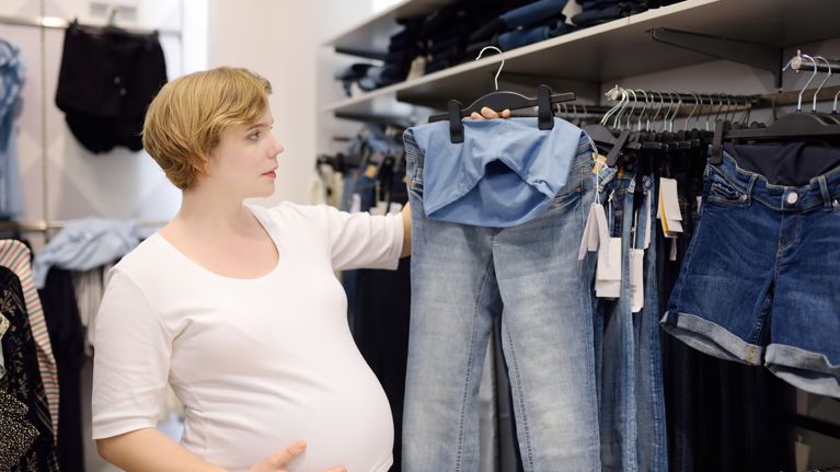 Young pregnant woman choosing clothes in the store for pregnancy