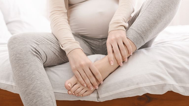Pregnant woman massaging her swollen foot sitting on bed
