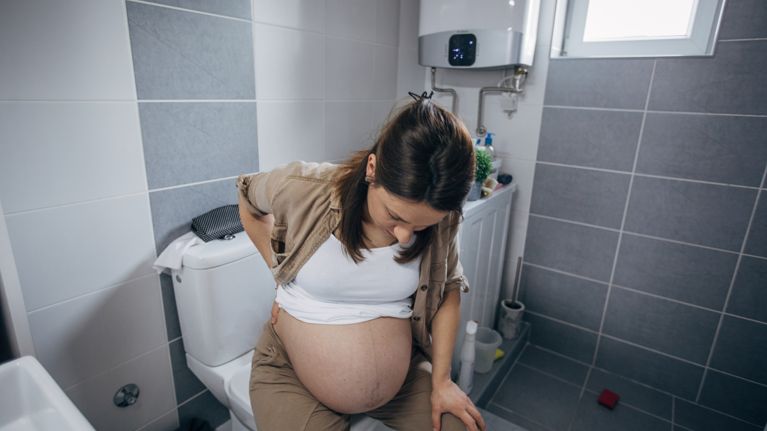 Pregnant woman in pain sitting on toilette in bathroom
