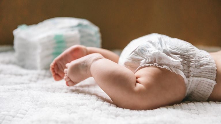 A baby in a diaper at the age of two months and a stack of diapers.