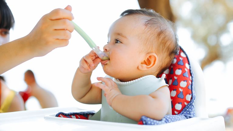 Modern mother spoon feeding her adorable daughter with a homemade mashed baby food