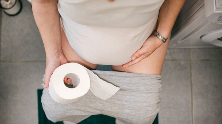 Pregnant woman holding toilet paper and using toilet
