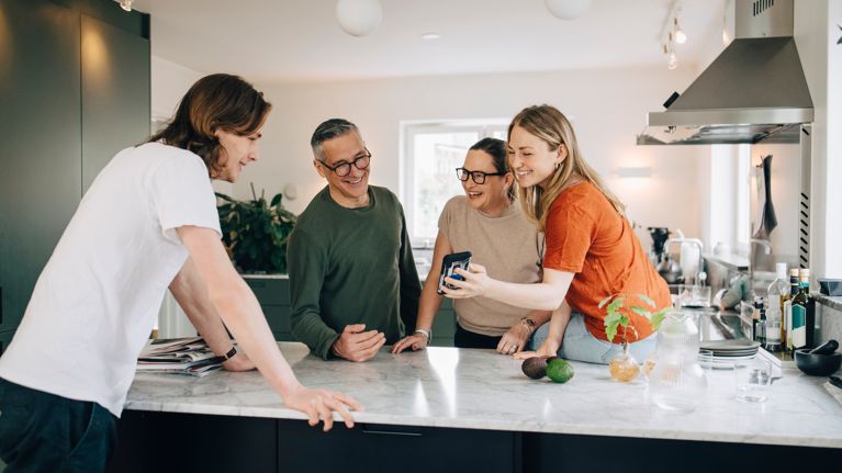 Young woman showing smart phone to brother and parents in kitchen at home