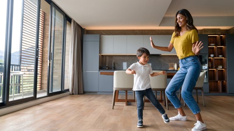 Happy mother having fun dancing with her son at home and laughing 