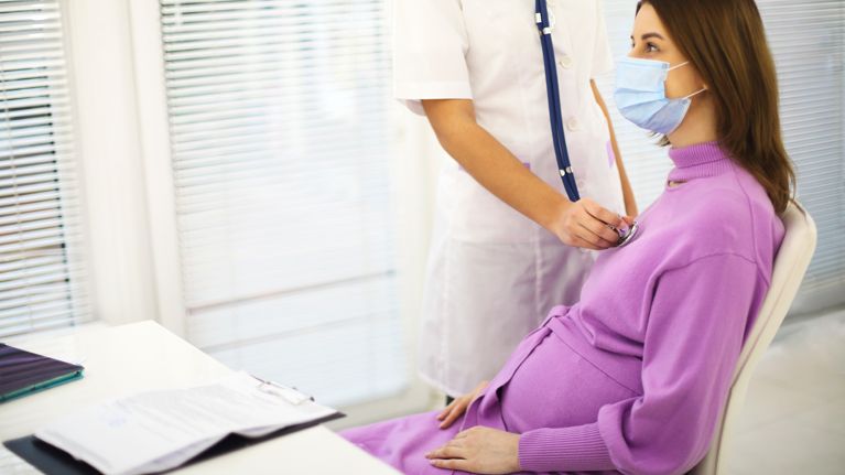 Doctor listening to pregnant woman heartbeat with stethoscope during prenatal care appointment in hospital