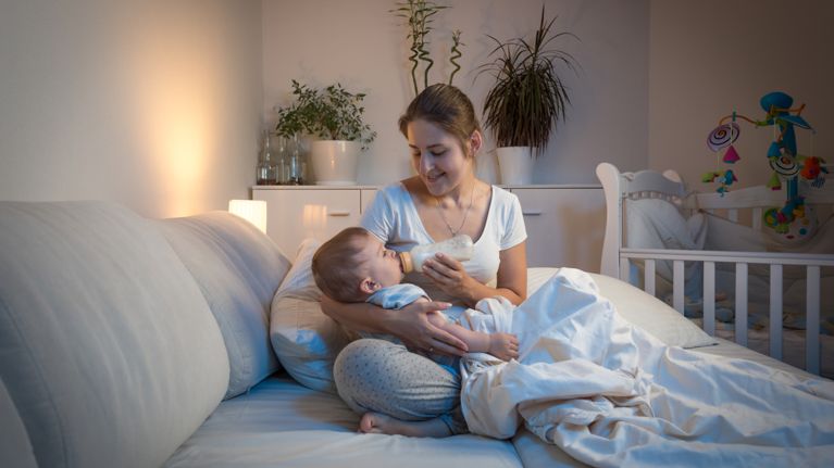 Portrait of beautiful young mother giving milk to her baby boy in bed at night