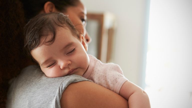 Close Up Of Mother Cuddling Sleeping Baby Daughter At Home