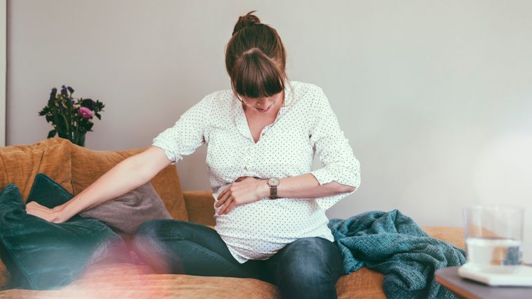Expectant mother timing her contractions while sitting on couch at home