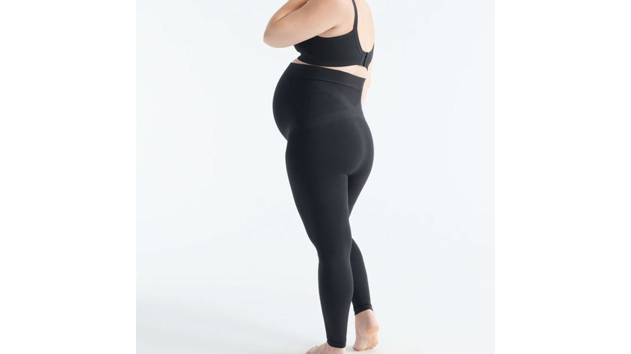 A side view of a pregnant woman in a pair of black leggings that go over her belly and have build-in support lines