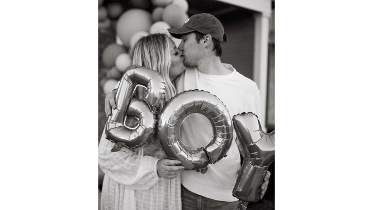 a couple kisses while holding balloons that say BOY