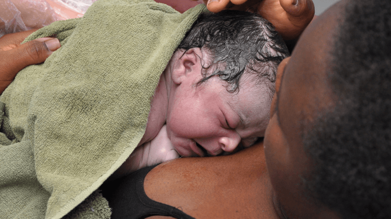 woman immediately after giving birth holding her new baby in a towel