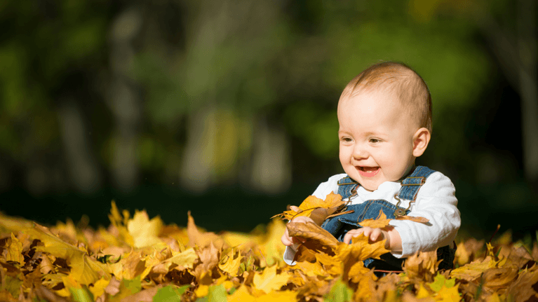 Baby sitting in a pile of leaves smiling
