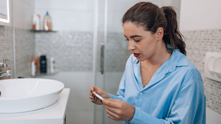 woman looking down at a pregnancy test looking somber