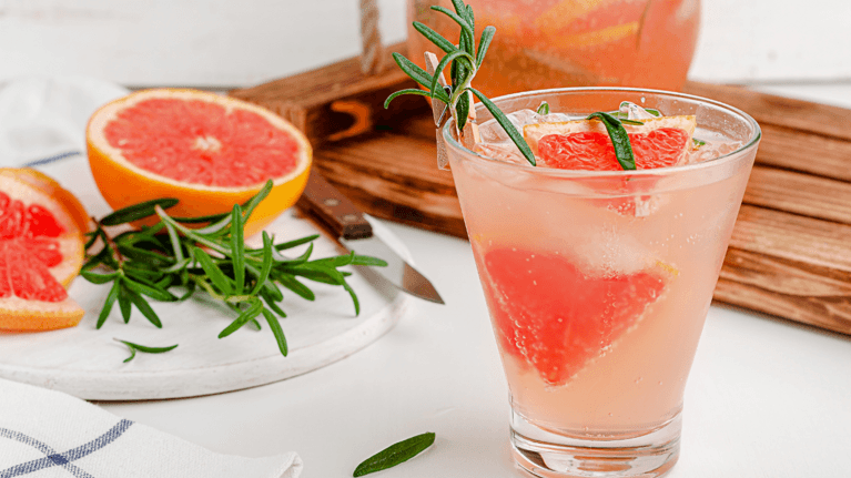fancy grapefruit mocktail on a table with rosemary and slices of grapefruit next to it