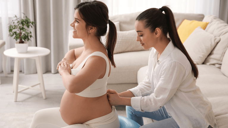 woman in labour sitting on a birthing ball with a support person with her