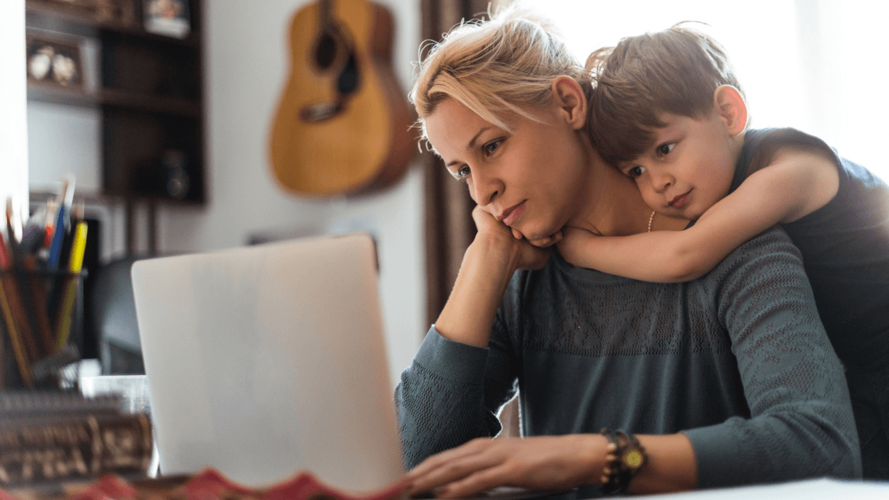mom concerned looking at a computer while her son hugs her from behind