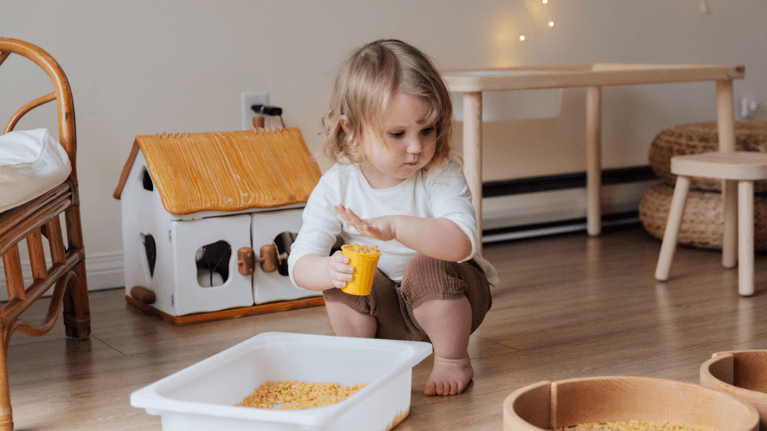 toddler playing with a bin of dry macaroni