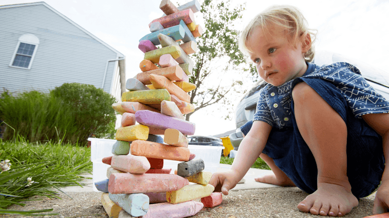 child sitting outside building a tower out of sidewalk chalk